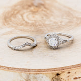 Shown here is "Eileen", a vintage-style moissanite women's engagement ring with a diamond halo, accents, and tracer, laying together. Many other center stone options are available upon request.