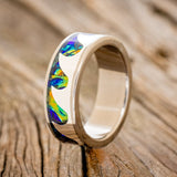 Shown here is "Poseidon", a custom, handcrafted men's wedding ring featuring ocean waves using pieces of silver and a black sea dichrolam inlay, upright facing left. Additional inlay options are available upon request.