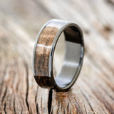 Shown here is "Rainier", a custom, handcrafted men's wedding ring featuring dark maple wood inlay, shown here on a fire-treated black zirconium band, upright facing left. Additional inlay options are available upon request.