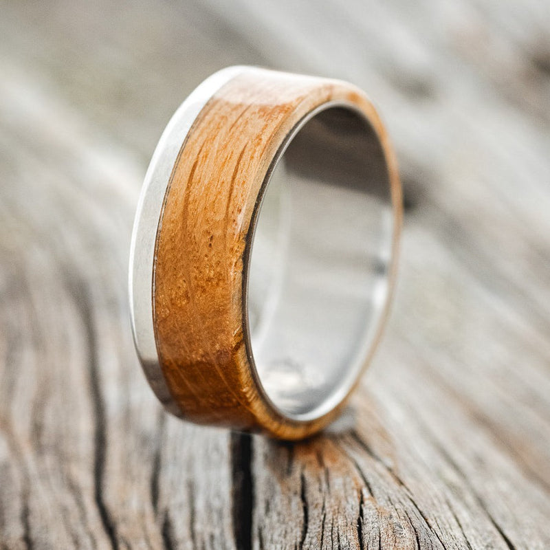 Shown here is "Ezra", a custom, handcrafted men's wedding ring featuring a whiskey barrel oak overlay, upright facing left. Additional inlay options are available upon request.