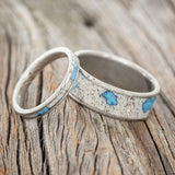 Shown here is a matching wedding band set featuring "Eterna" & "Rainier", laying together. "Rainier" is a handcrafted wide wedding band featuring antler and accented turquoise inlay. "Eterna" is a stacking-style wedding band featuring antler and accented turquoise inlay.