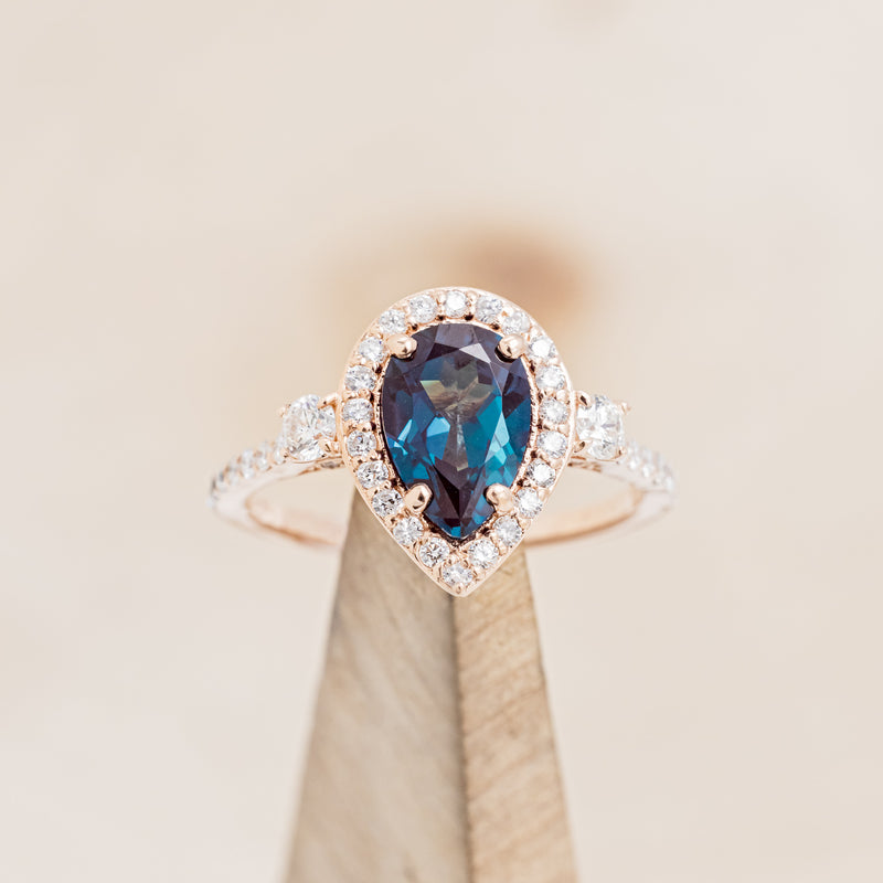 Shown here is "KB", a lab-created alexandrite women's engagement ring with diamond halo & accents, on stand front facing. Many other center stone options are available upon request.