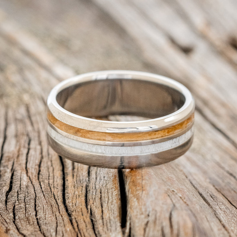 Shown here is "Cosmo", a custom, handcrafted men's wedding ring featuring whiskey barrel oak and antler inlays, laying flat. Additional inlay options are available upon request.