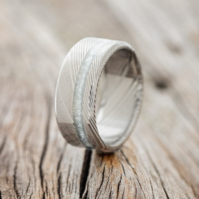 Shown here is "Vertigo", a custom, handcrafted men's wedding ring featuring a diamond dust inlay, shown here set in a Damascus Steel, upright facing left. The inlay is called Diamond dust, which is a unique blend of materials that allows for a beautiful shine of color. Additional inlay options are available upon request.