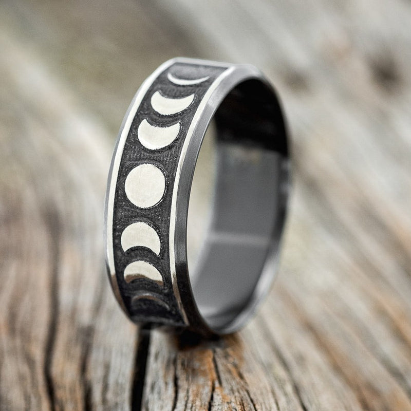 Shown here is "Lucian", a handcrafted, custom embossed men's wedding ring featuring the phases of the moon, upright facing left. This ring is pictured in black zirconium, giving it a higher contrast between embossment and engraving than other metal types will provide. It can be customized to feature just about any embossed design you can dream up!