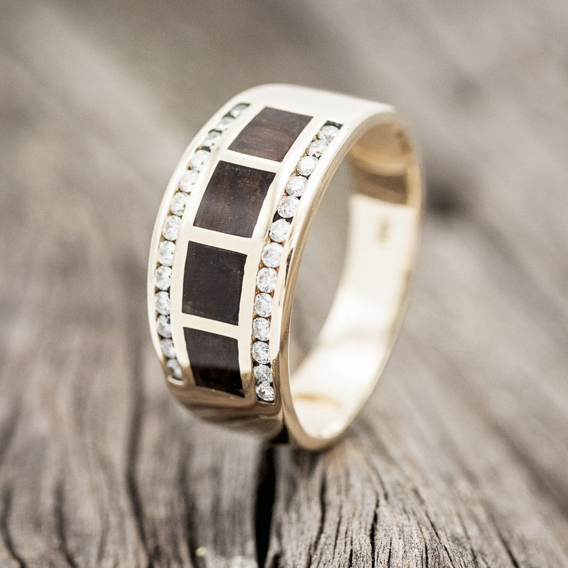 Shown here is "Aldo", a custom, handcrafted men's wedding ring featuring a 14K yellow gold band with 26 diamonds and ironwood, upright facing left. Additional inlay options are available upon request.