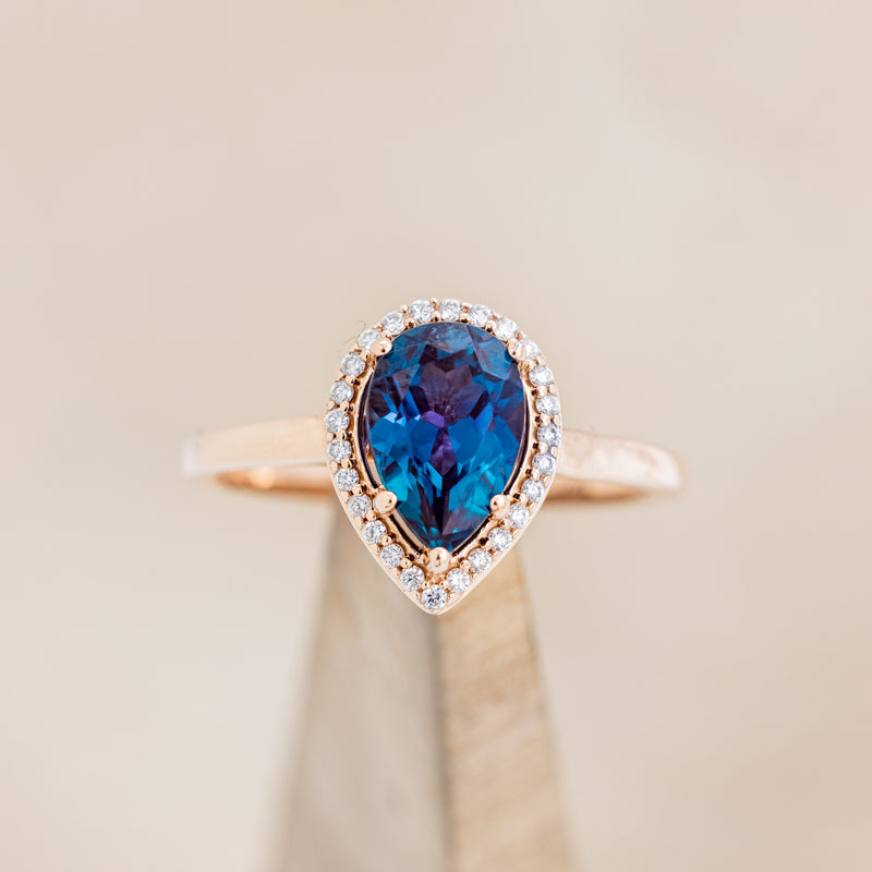 Shown here is "Clariss", a bridal suite-style lab-created alexandrite women's engagement ring with a diamond halo, on stand front facing. Many other center stone options are available upon request.