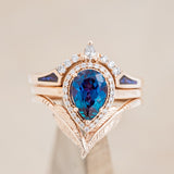 Shown here is "Clariss", a bridal suite-style lab-created alexandrite women's engagement ring with a diamond halo, "Fala" tracer, and "Sama" tracer, on stand front facing. Many other center stone options are available upon request. 