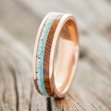 Shown here is "Rainier", a custom, handcrafted men's wedding ring featuring an ironwood, turquoise, and antler inlay on a 14K gold band, upright facing left. Additional inlay options are available upon request.