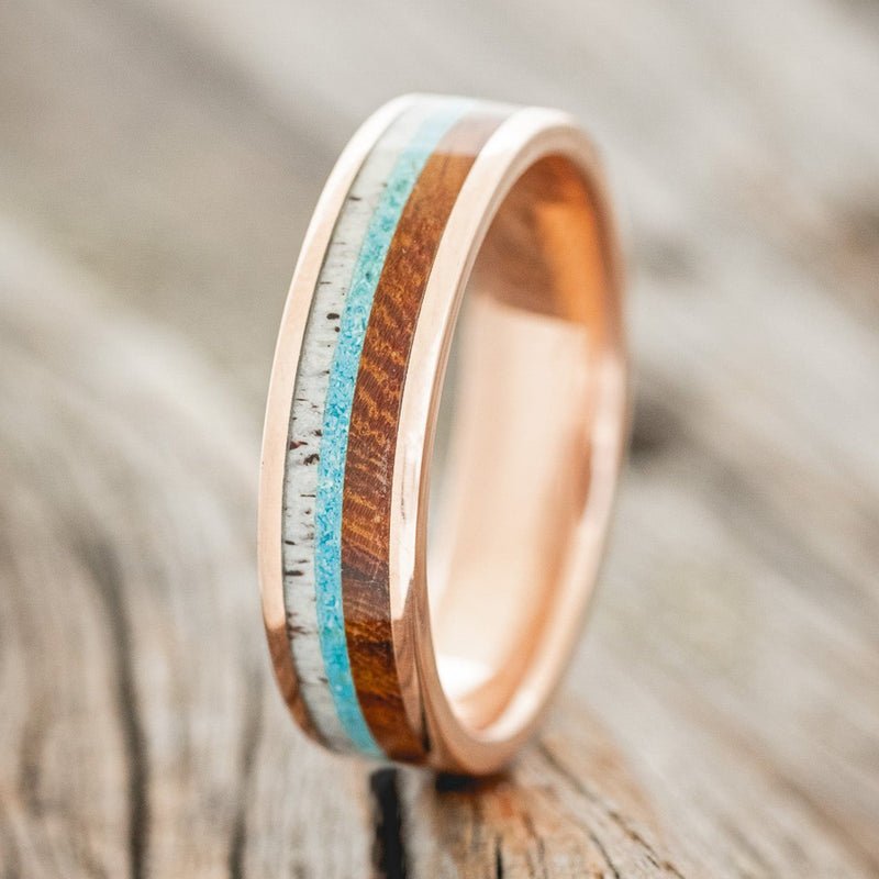 Shown here is "Rainier", a custom, handcrafted men's wedding ring featuring an ironwood, turquoise, and antler inlay on a 14K gold band, upright facing left. Additional inlay options are available upon request.