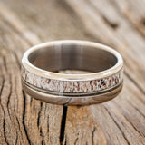 Shown here is "Tanner", a custom, handcrafted men's wedding ring featuring a naturally shed elk antler and guitar string inlay, laying flat. Additional inlay options are available upon request.
