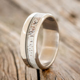 Shown here is "Tanner", a custom, handcrafted men's wedding ring featuring a naturally shed elk antler and guitar string inlay, upright facing left. Additional inlay options are available upon request.