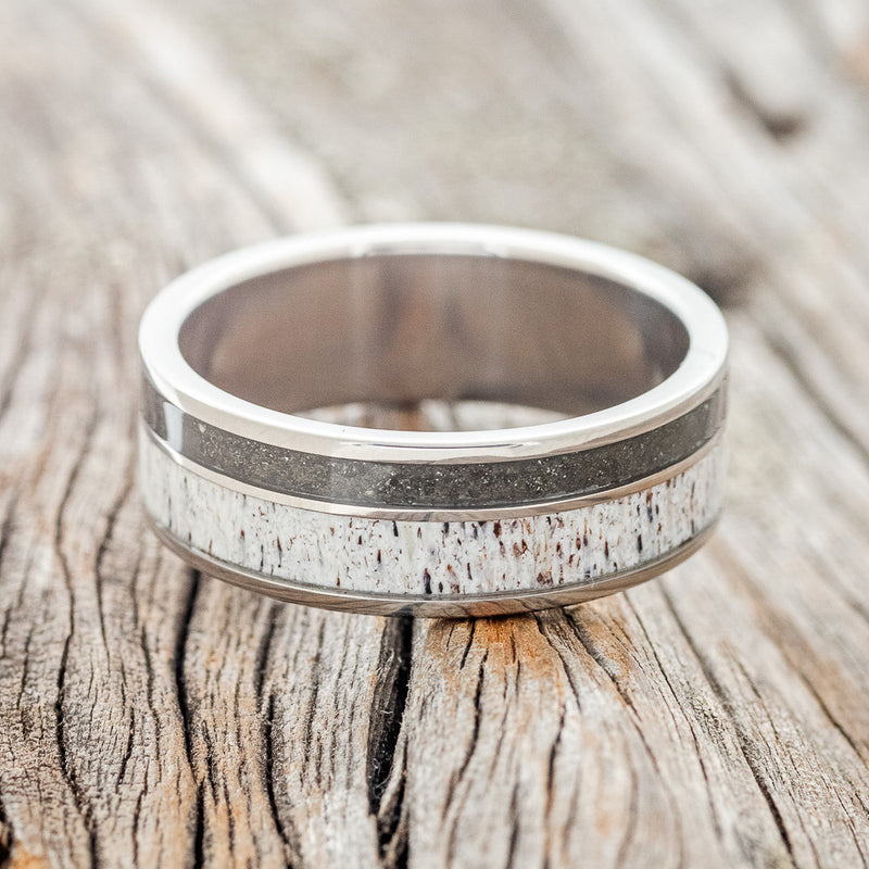 Shown here is "Raptor", a custom, handcrafted men's wedding ring featuring elk antler and iron ore inlays on a titanium band, laying flat. Additional inlay options are available upon request.