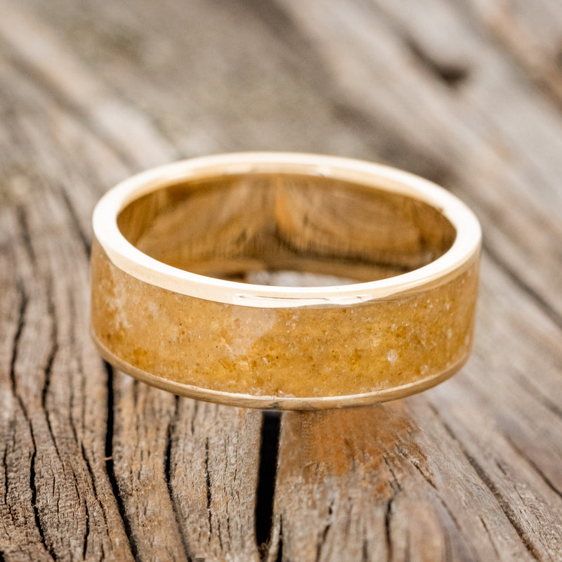 Shown here is "Rainier", a handcrafted men's wedding ring featuring an amber inlay on a 14K gold band, laying flat. Additional inlay options are available upon request.