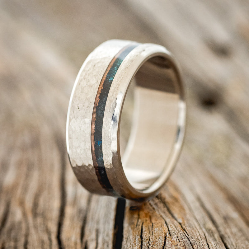 Shown here is "Vertigo", a custom, handcrafted men's wedding ring featuring patina copper inlay on a hammered band, upright facing left. 