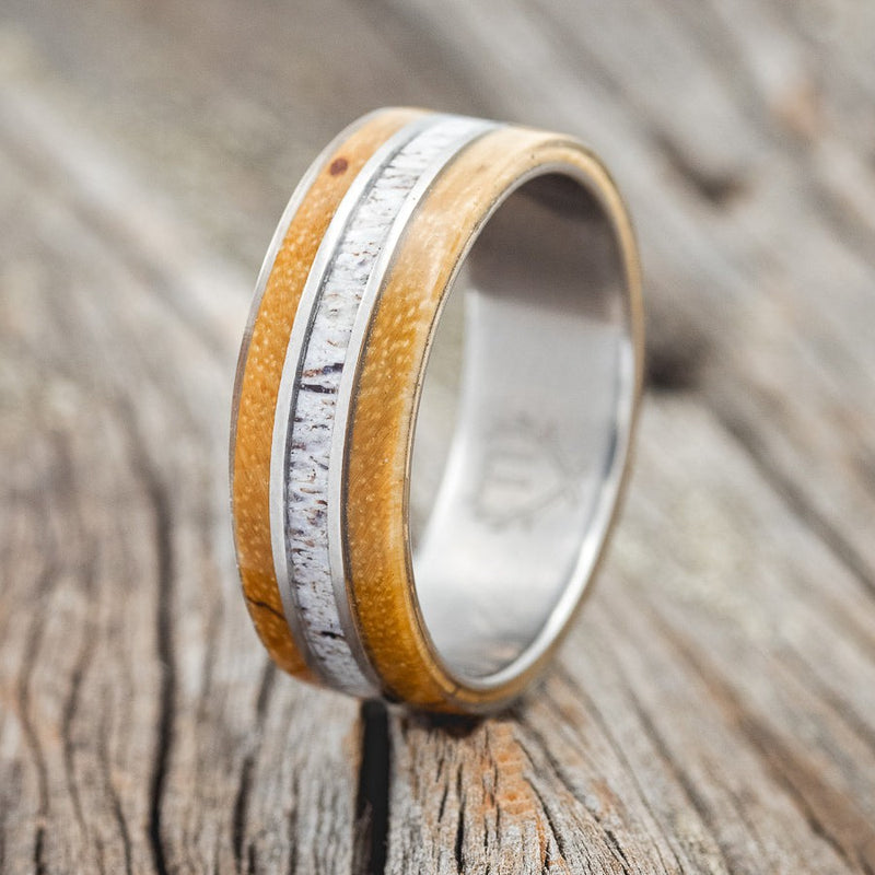 Shown here is "Glen", a custom, handcrafted men's wedding ring featuring spalted maple, antler, shown here on a titanium band, upright facing left. Additional inlay options are available upon request.