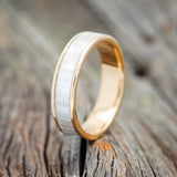 Shown here is "Rainier", a handcrafted men's wedding ring featuring a hand-set and shaped mother of pearl inlay on a 14K gold band, upright facing left. Additional inlay options are available upon request.