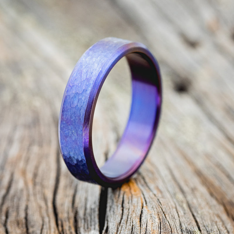 Shown here is a handcrafted men's wedding ring featuring a fire-treated titanium band with a hammered finish, upright facing left.