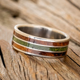 Shown here is "Rio", a custom, handcrafted men's wedding ring featuring 3 channels with redwood and moss inlays on a titanium band, tilted left. Additional inlay options are available upon request.