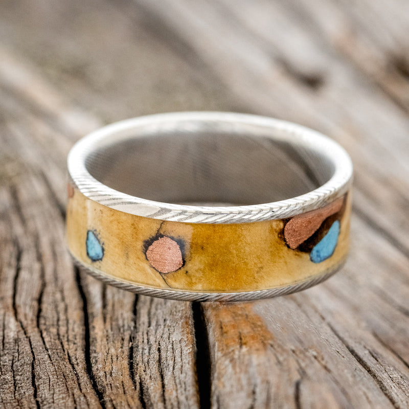 Shown here is "Rainier", a handcrafted men's wedding ring featuring buckeye burl wood with turquoise and copper inlays set into the burls, laying flat.