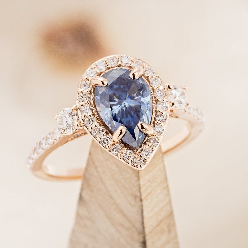 shown here is The "Indigo", a halo-style pear shaped moissanite women's engagement ring with delicate and ornate details and is available with many center stone options-Blue Moissanite Engagement Ring With Diamond Halo & Accents - Staghead Designs