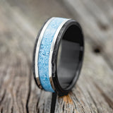 Shown here is "Hollis", a custom, handcrafted men's wedding ring featuring hammered, fire-treated black zirconium band with turquoise & 14K white gold inlays, upright facing left. Additional inlay options are available upon request.
