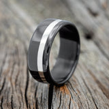 Shown here is "Vertigo", a handcrafted men's wedding ring featuring shown here on a fire-treated black zirconium band with a silver inlay, upright facing left. Additional inlay options are available upon request.
