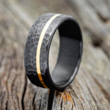 Shown here is a handcrafted men's wedding ring featuring an offset 14K yellow gold inlay with a hammered finish, upright facing left. Shown here set on a fire-treated black zirconium wedding band. Additional inlay options are available upon request.