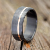 Shown here is a handcrafted men's wedding ring featuring a 14K rose gold inlay on a fire-treated black zirconium band with a brushed finish, upright facing left. Additional inlay options are available upon request.