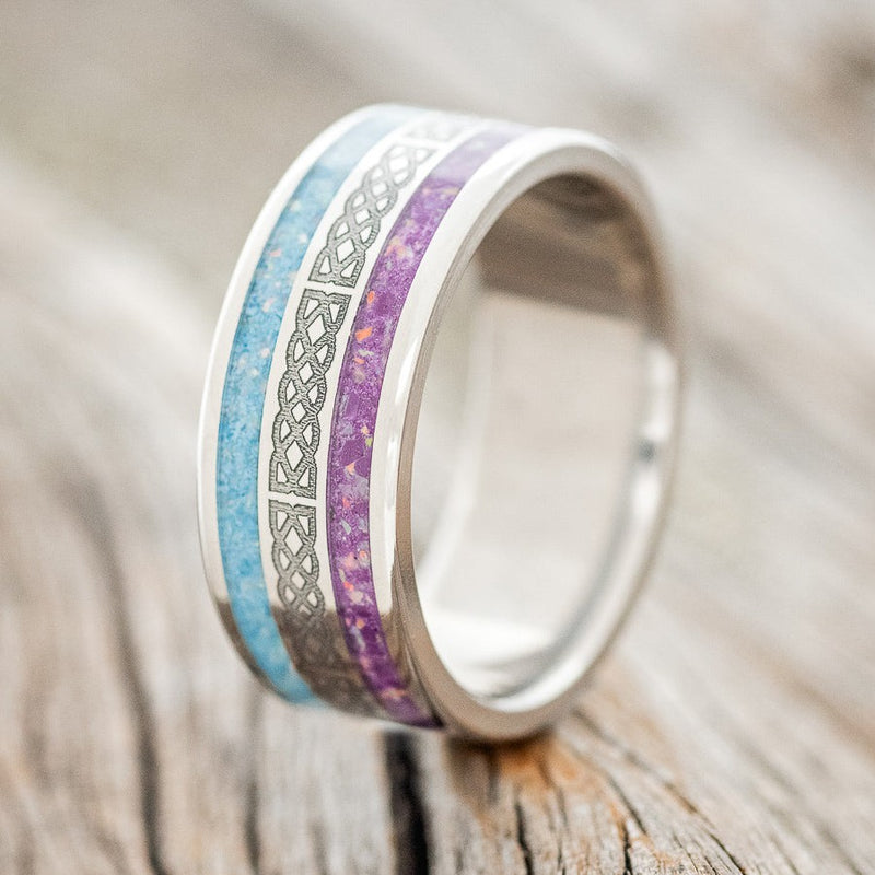 Shown here is "Ryder", a custom engraved Celtic sailor's knot-patterned men's wedding ring featuring sugilite and turquoise inlays, upright facing left. Both the sugilite and the turquoise inlays have been mixed with opal. Additional inlay options are available upon request.