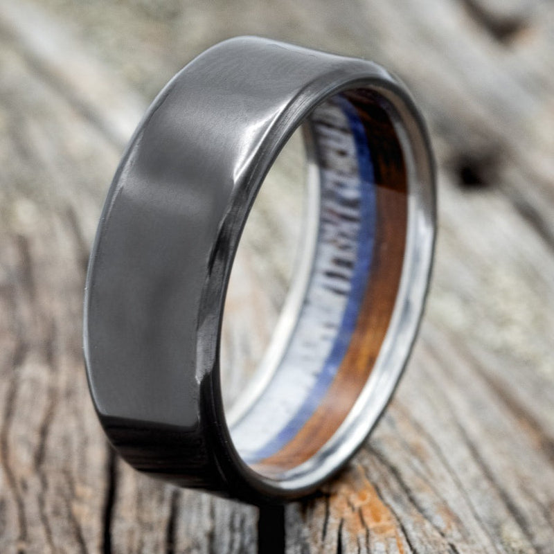 Shown here is "Banner", a custom, handcrafted men's wedding ring featuring lapis lazuli,  whiskey barrel wood, and naturally shed antler lining, shown here on a black zirconium band, upright facing left. Additional inlay options are available upon request.