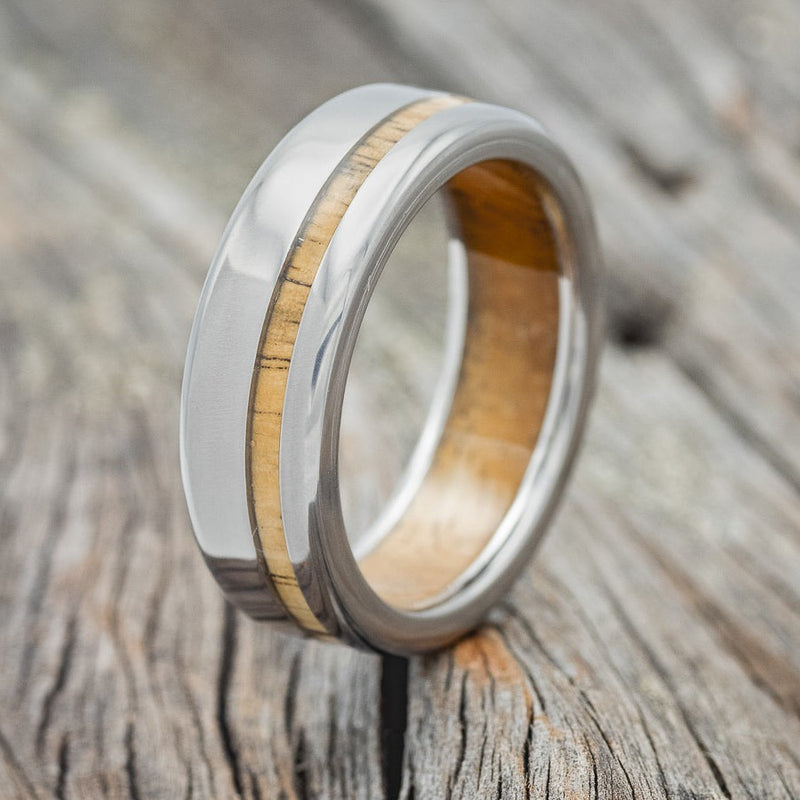 Shown here is "Vertigo", a handcrafted men's wedding ring featuring spalted maple lining set on a titanium band with a spalted maple inlay, upright facing left. Additional inlay options are available upon request.