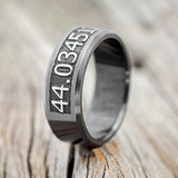 Shown here is "Path finder", a handcrafted, custom embossed coordinates men's wedding band, upright facing left. This ring is pictured in black zirconium, giving it a higher contrast between embossment and engraving than other metal types will provide. It can be customized to feature just about any embossed design you can dream up. 