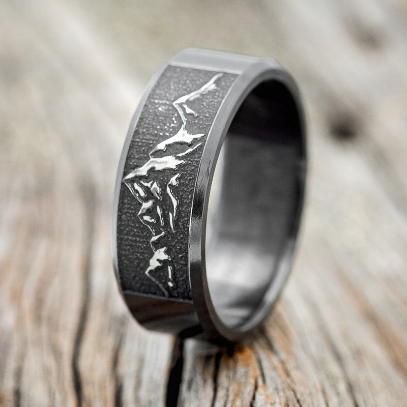 Shown here is "Path finder", a handcrafted, custom embossed mountain men's wedding band, upright facing left. This ring is pictured in black zirconium, giving it a higher contrast between embossment and engraving than other metal types will provide. It can be customized to feature just about any embossed design you can dream up. 