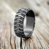 Shown here is "Parcel", a handcrafted, custom embossed men's wedding ring featuring a tire tread engraving, upright facing left. This ring is pictured in black zirconium giving it a higher contrast between embossment and engraving than other metal types will provide. It can be customized to feature just about any embossed design you can dream up.