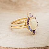 Shown here is "Rapunzel", an oval opal women's engagement ring with amethyst and tanzanite accents, facing right. Many other center stone options are available upon request.