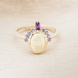 Shown here is "Rapunzel", an oval opal women's engagement ring with amethyst and tanzanite accents, front facing. Many other center stone options are available upon request.