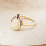 Shown here is "Rapunzel", an oval opal women's engagement ring with amethyst and tanzanite accents, facing left. Many other center stone options are available upon request.
