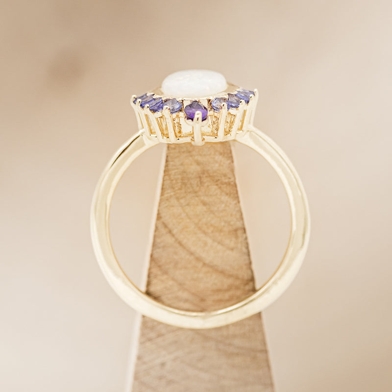 Shown here is "Rapunzel", an oval opal women's engagement ring with amethyst and tanzanite accents, side view on stand. Many other center stone options are available upon request.