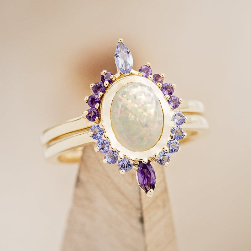 Shown here is "Rapunzel", an oval opal women's engagement ring with amethyst and tanzanite accents, on stand front facing. Many other center stone options are available upon request.  