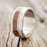 Shown here is "Raptor", a custom, handcrafted men's wedding ring featuring a mother of pearl and redwood inlays, upright facing left. Additional inlay options are available upon request.