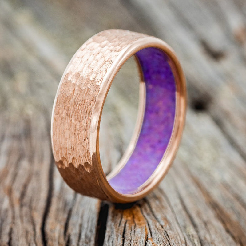 Shown here is a handcrafted men's wedding band shown on a 14K rose gold band with a sleepy lavender opal lining and a hammered finish, upright facing left. Additional inlay options are available upon request.