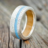 Shown here is "Vertigo", a handcrafted men's wedding ring featuring a whiskey barrel lining, a turquoise inlay, and a hammered finish, upright facing left. Additional inlay options are available upon request.