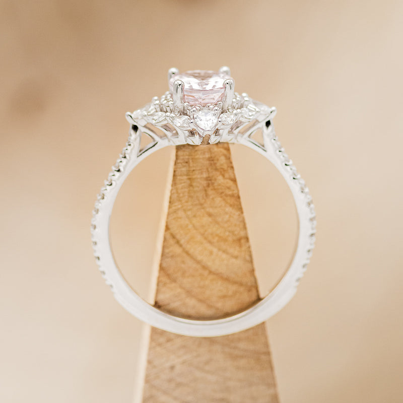 Shown here is "North Star", an oval morganite women's engagement ring with a diamond halo and diamond accents, side view on stand. Many other center stone options are available upon request.