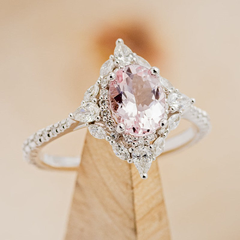 Shown here is "North Star", an oval morganite women's engagement ring with a diamond halo and diamond accents, on stand facing slightly right. Many other center stone options are available upon request. 