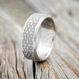 Shown here is a handcrafted men's wedding ring featuring a solid band with Celtic love knot engravings, upright facing left. 