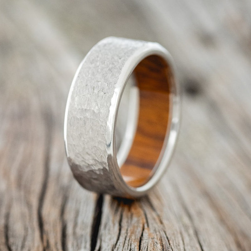 Shown here is a handcrafted men's wedding ring featuring an ironwood lining and a hammered finish shown here on a titanium band, upright facing left. Additional inlay options are available upon request.