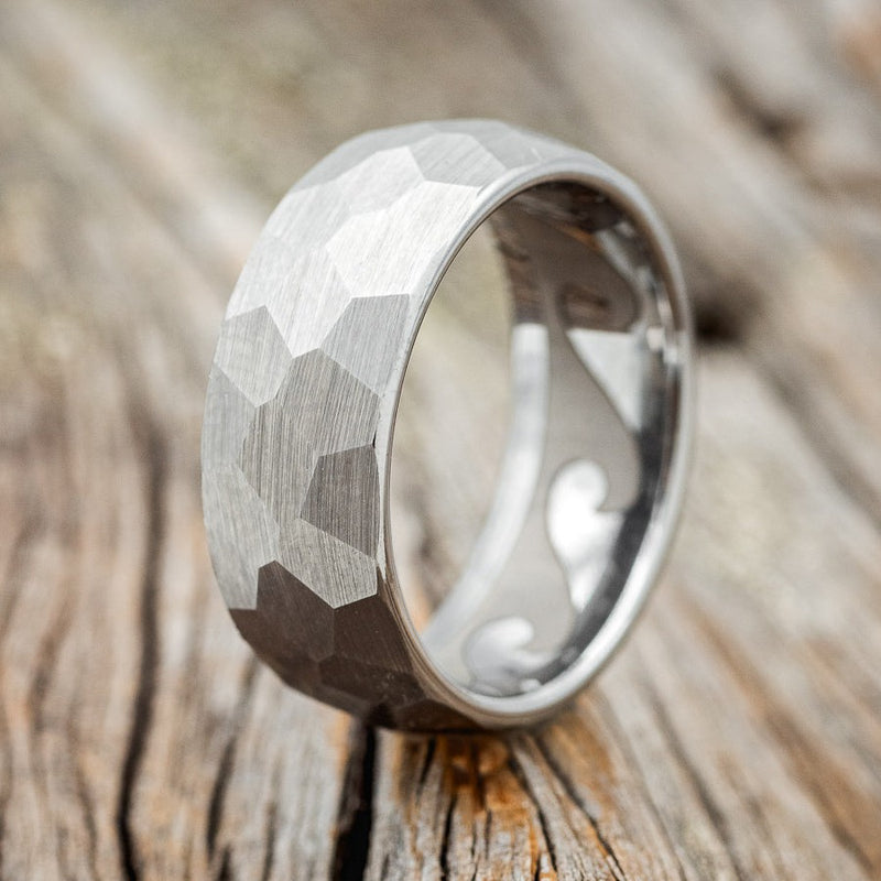 Shown here is a handcrafted men's wedding ring featuring a faceted band with a wave engraved lining, upright facing left. Additional engraved options are available upon request.