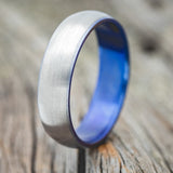 Shown here is a handcrafted men's wedding ring featuring a fire-treated titanium band with a brushed finish and a domed profile, upright facing left. 