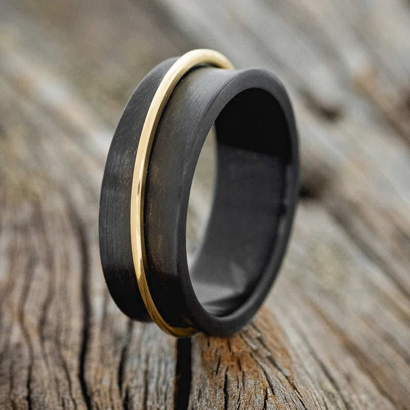 Shown here is "Rotary", a handcrafted concave men's wedding ring featuring a free-spinning 14K yellow gold band, upright facing left. Shown here set on a black zirconium wedding band. Additional inlay options are available upon request.